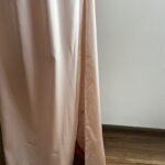 Dlhé ružové spoločenské šaty s luxusným leskom očaria výraznými volánmi na ramenách a zavinovacím výstrihom, ktorý elegantne tvaruje dekolt. Hladká sukňa s rozparkom dodáva modelu ženskosť a voľnosť pohybu. Perfektná voľba na svadby, oslavy či večerné príležitosti.