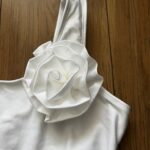 Štýlové biele dvojdielne plavky s asymetrickým ramienkom a ozdobnou 3D kvetinou sú dokonalou kombináciou trendu a jemnej elegancie pre mladé slečny. Vrchný diel zdobí decentný zlatý nápis značky, ktorý dodáva kúsku exkluzívny nádych. Pohodlný strih s vyšším spodným dielom zabezpečí komfort pri plávaní aj opaľovaní.